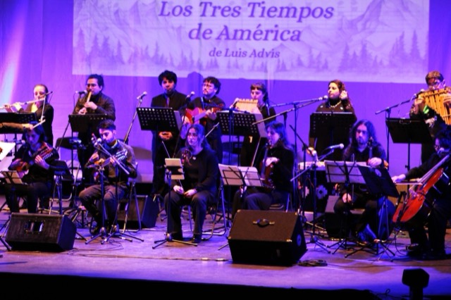 Ensamble Clase completo en el escenario, con el título «Los Tres Tiempos de América, de Luis Advis» proyectado al fondo.