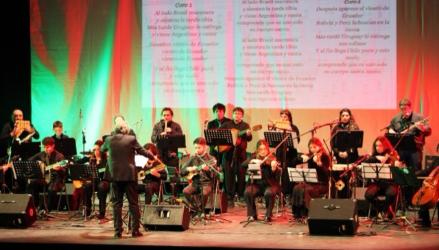 El escenario completo bajo luces verdes y rojas, con los textos de los tres coros proyectados al fondo.
