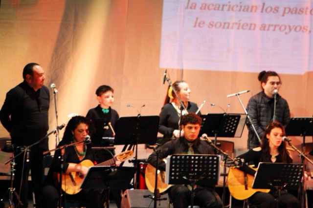 Cantantes e instrumentistas de Ensamble Clase con los versos de la obra proyectados sobre el telón.